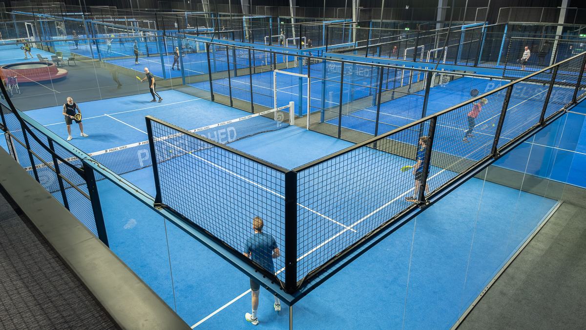 Players on the courts at a busy indoor padel club, seen from the viewing balcony