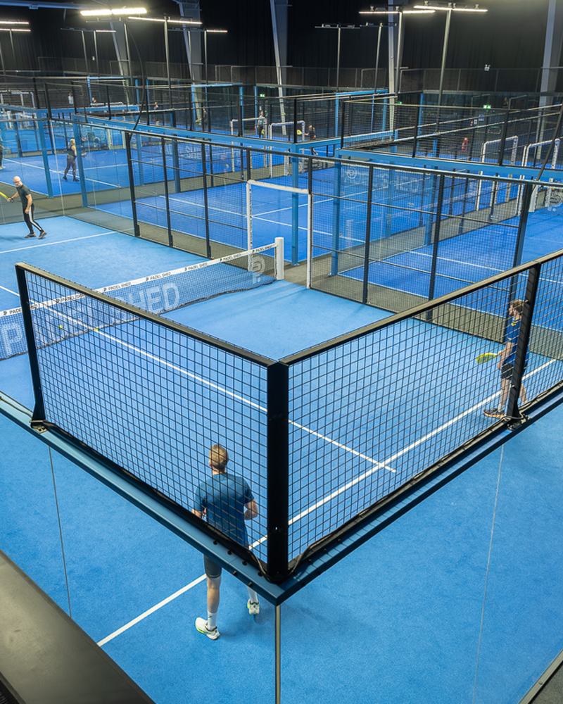 Players on the blue courts of an indoor padel club