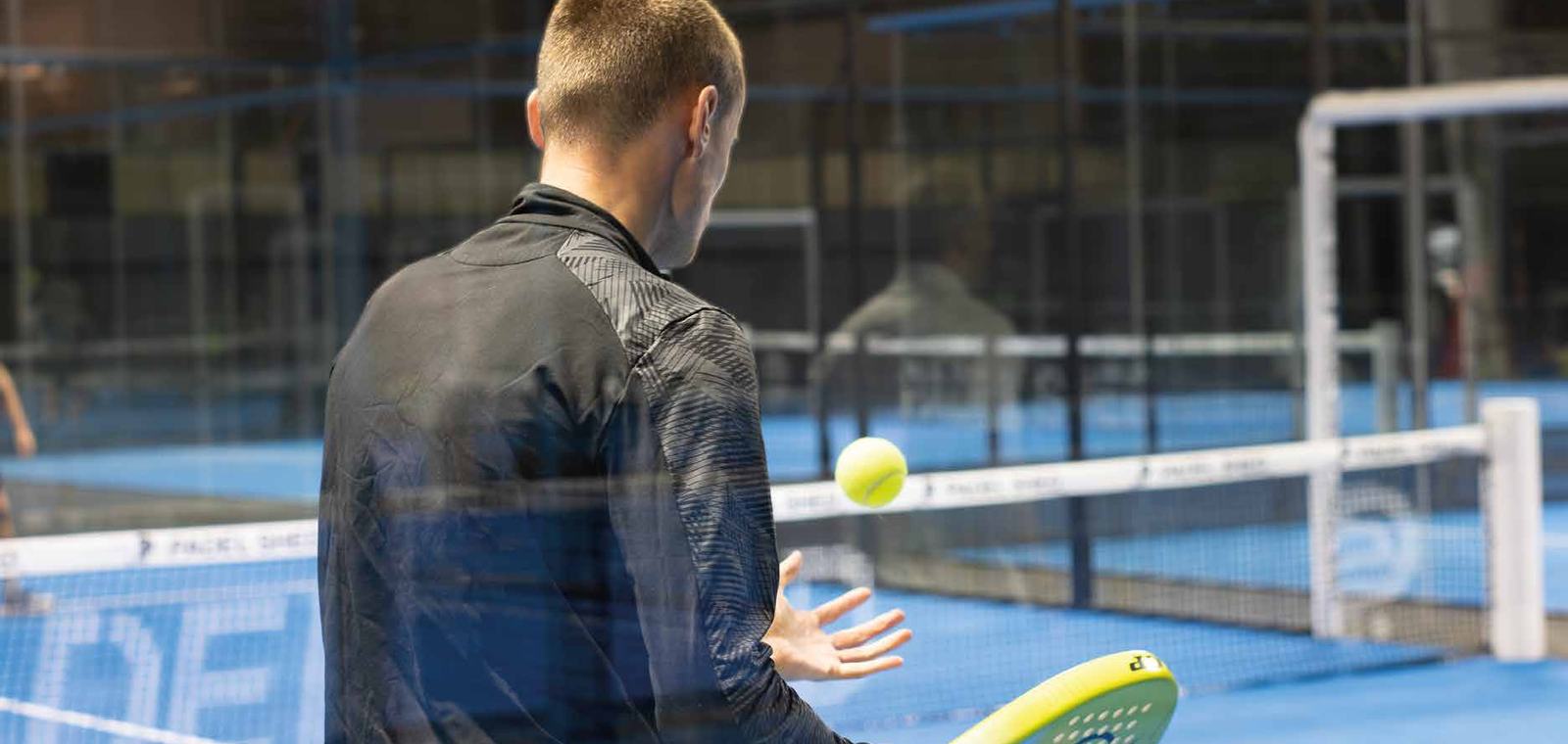 A padel player waiting to serve on an indoor court